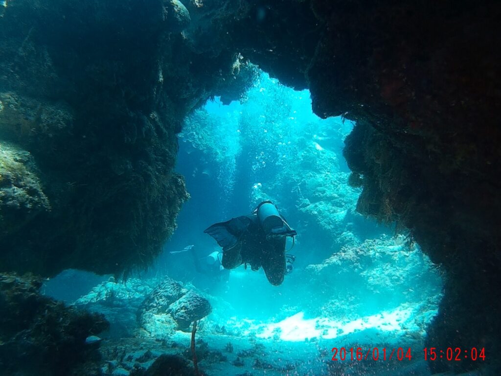 Un buceador cruza un arco de coral oscuro en Palancar, con la arena blanca iluminada por el sol detrás de él