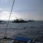 Tres bancas de buceo fondeadas en Monad Shoal bajo un cielo gris de madrugada, vistas desde la cubierta de otro barco