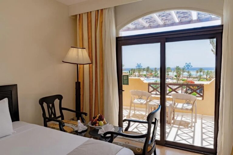 Una habitación con dos sillones de madera oscura, abierta a un balcón frente a la piscina y el mar