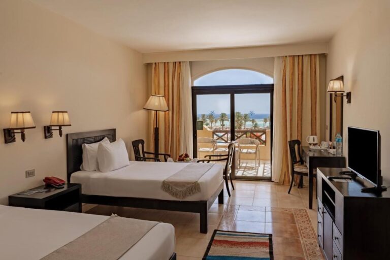 Una habitación con dos camas, televisión, escritorio y balcón frente al mar