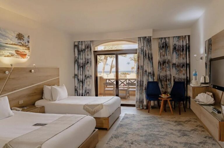 Una habitación con dos camas, dos sillones azules y una puerta de vidrio que da al balcón