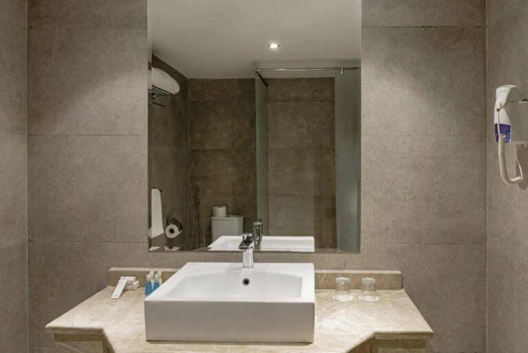 Un baño con lavabo cuadrado, espejo grande y secador de pelo