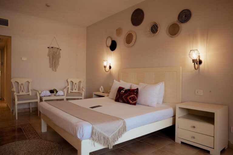 Una habitación con cama grande, cestas trenzadas en la pared y dos sillas blancas