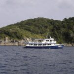 Un barco de crucero azul y blanco fondeado frente a una isla de las Similan, con sus bloques de granito gris a ras del agua bajo la selva