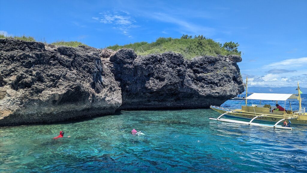 El acantilado calizo gris y erosionado de la isla Pescador, dos nadadores con máscara y tubo y una banca amarilla en un agua turquesa