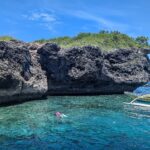 El acantilado calizo gris y erosionado de la isla Pescador, dos nadadores con máscara y tubo y una banca amarilla en un agua turquesa