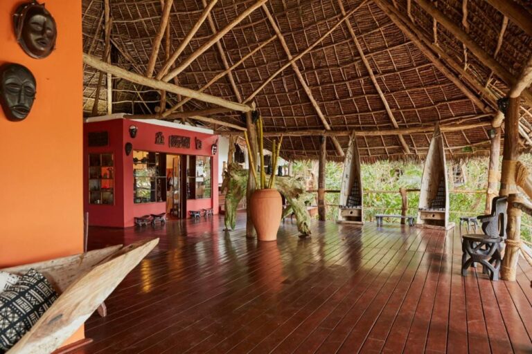 Un gran espacio abierto bajo un techo de paja, con suelo de madera y máscaras africanas