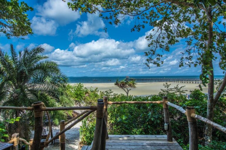 Vista desde una terraza de madera sobre una amplia playa de arena y un largo embarcadero