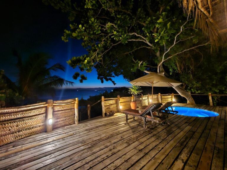 Una terraza de madera iluminada por la noche, con una piscina pequeña, dos tumbonas y una sombrilla
