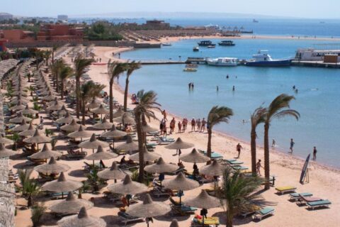 La playa del Giftun Azur Resort, sus sombrillas de paja y sus palmeras, con un muelle y barcos al fondo