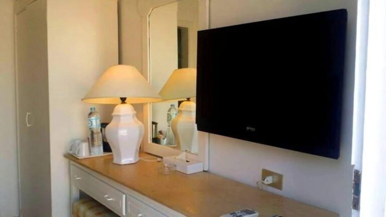 Una cómoda con una lámpara blanca, un espejo y un televisor de pared