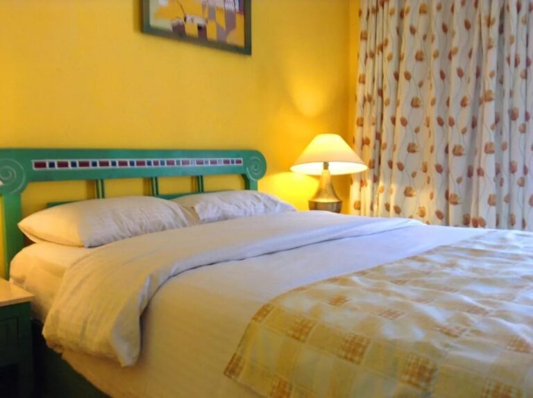 Una cama con cabecera verde decorada con mosaico, contra una pared amarilla