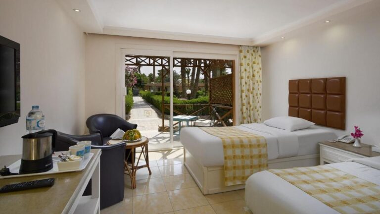 Una habitación con dos camas y dos sillones negros, abierta a una terraza y al jardín