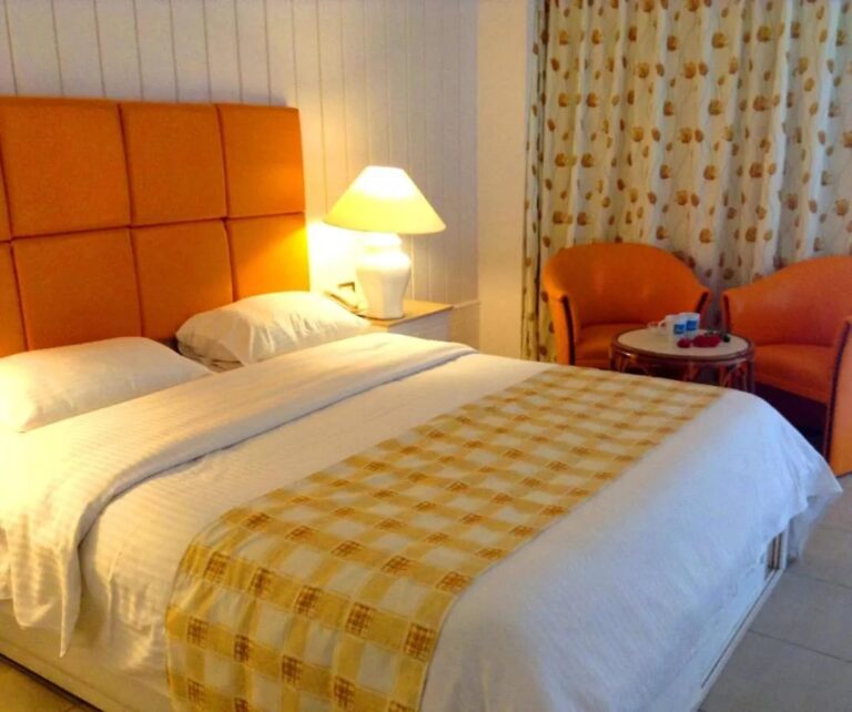 Una cama grande con cabecera naranja, dos sillones naranjas y una mesita redonda