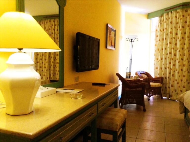 Una habitación de paredes amarillas, con escritorio, televisor y dos sillones de ratán junto a la ventana