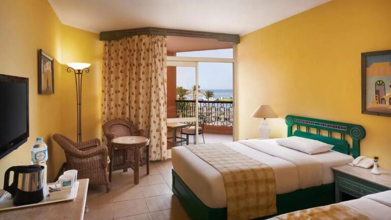 Una habitación de paredes amarillas con dos camas y un balcón frente al mar