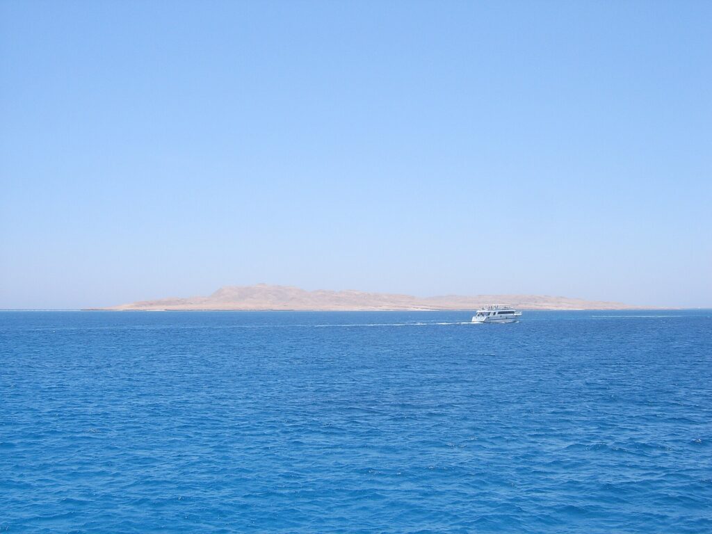 La isla plana y desértica de Giftun Soraya vista desde el mar, con un barco de buceo blanco que pasa por delante