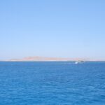 La isla plana y desértica de Giftun Soraya vista desde el mar, con un barco de buceo blanco que pasa por delante