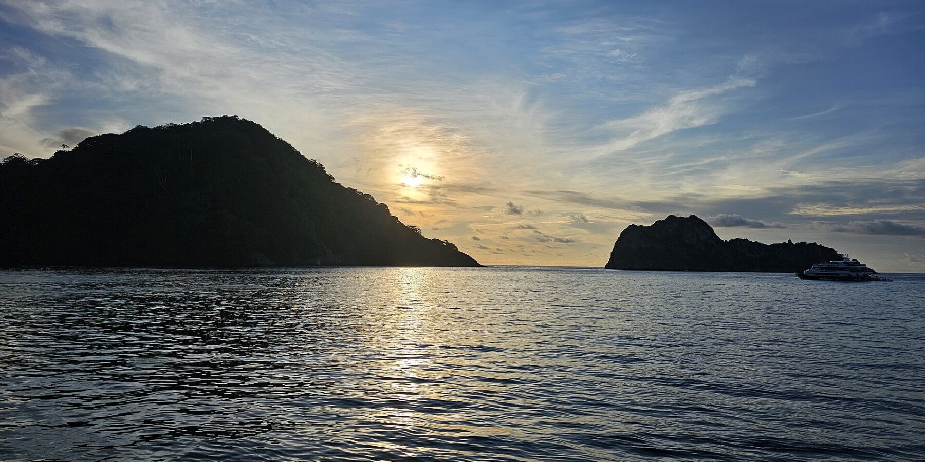 La isla del Coco a contraluz al atardecer, con un barco de crucero fondeado a la derecha y el mar en calma