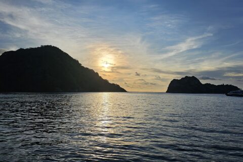 La isla del Coco a contraluz al atardecer, con un barco de crucero fondeado a la derecha y el mar en calma