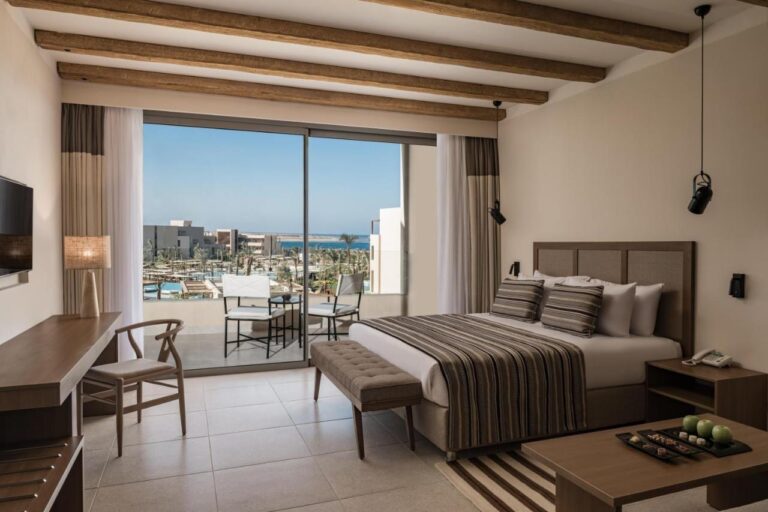 Una habitación con cama grande y balcón, con vista a las piscinas y al mar Rojo