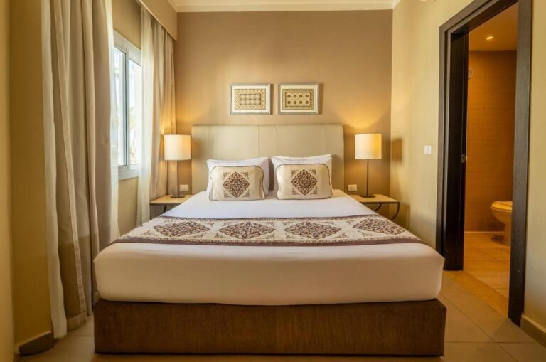 Una habitación con cama grande entre dos lámparas, con la puerta del baño abierta