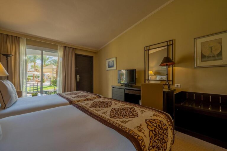 Una habitación con dos camas y una puerta de vidrio que da al jardín y a las palmeras