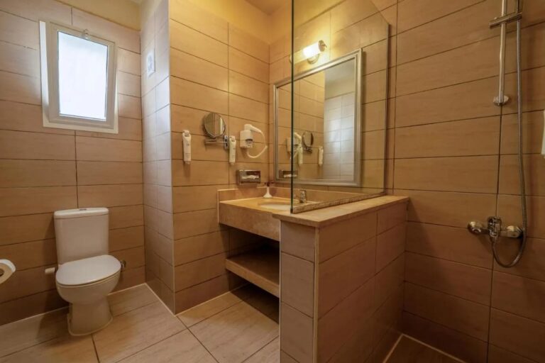 Un baño con una ventana pequeña, un lavabo y una ducha tras una mampara de vidrio