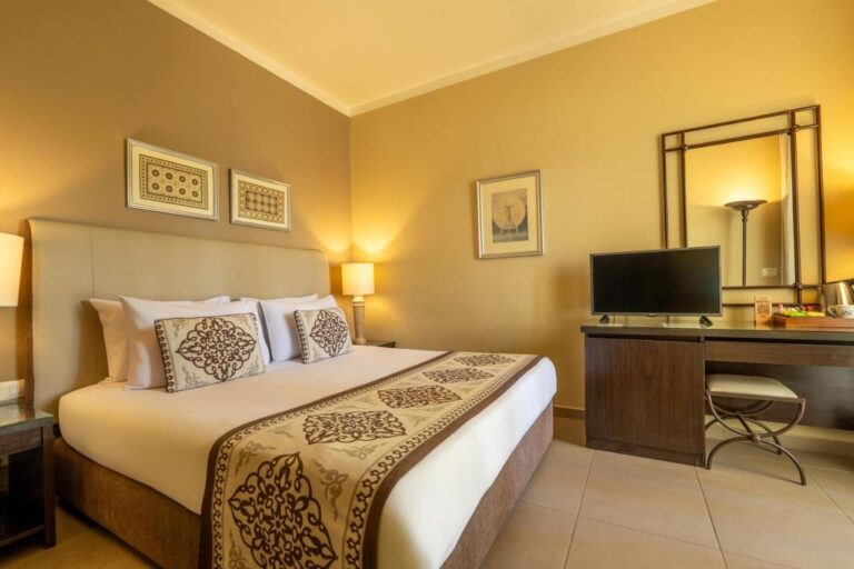 Una habitación con cama grande, un escritorio, un televisor y un espejo grande