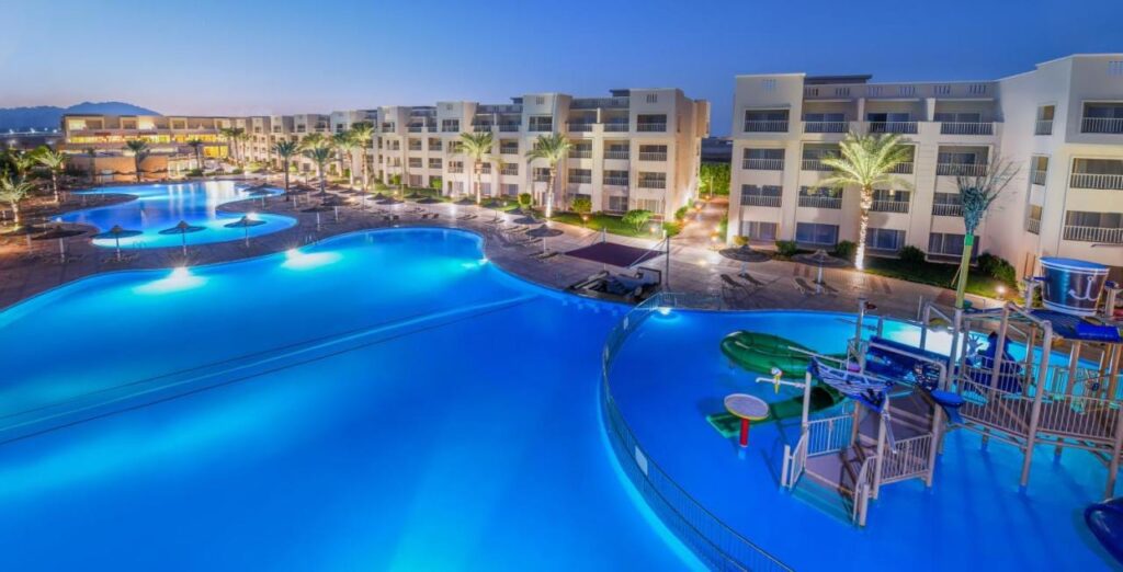 Las piscinas iluminadas del JAZ Soma Beach al anochecer, entre los edificios y las palmeras