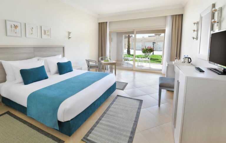 Una habitación con cama grande y muebles claros, abierta a una terraza y a un césped con flores