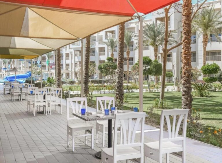 La terraza de un restaurante bajo toldos de vela, frente al jardín y las palmeras