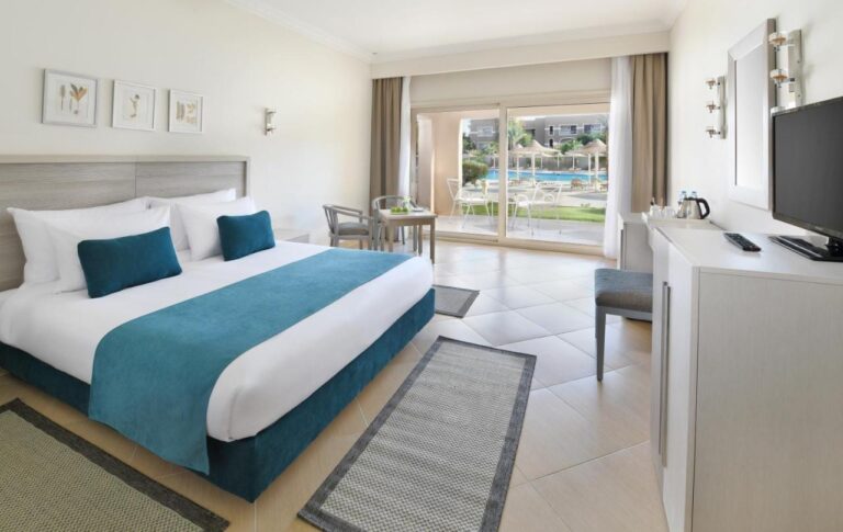 Una habitación con cama grande y muebles claros, abierta a una terraza frente a la piscina