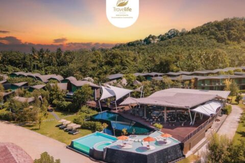 Vista aérea del Kalima Resort Khao Lak al atardecer, con sus piscinas y sus techos curvos al pie de una colina boscosa