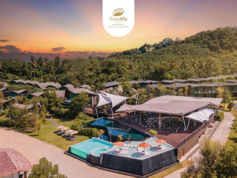 Vista aérea del Kalima Resort Khao Lak al atardecer, con sus piscinas y sus techos curvos al pie de una colina boscosa