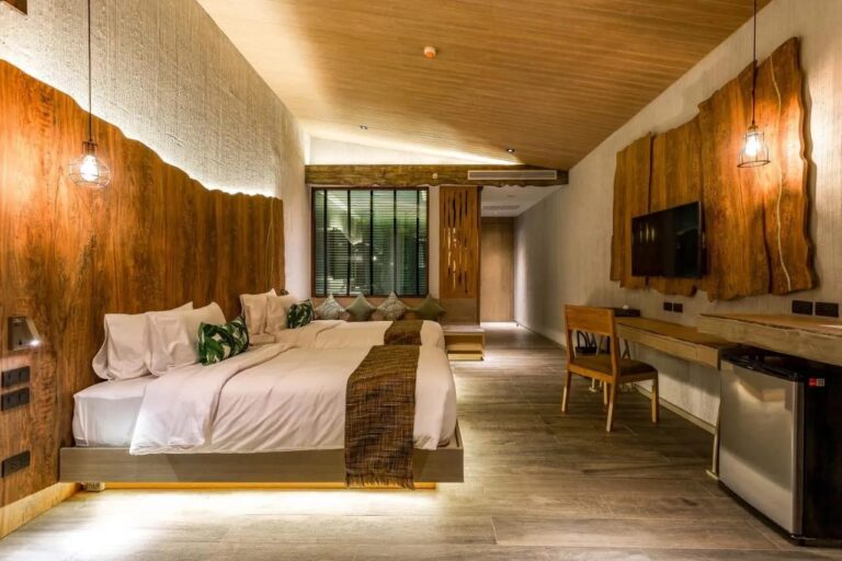 Una habitación con dos camas, cabecera de madera rústica, escritorio y televisor