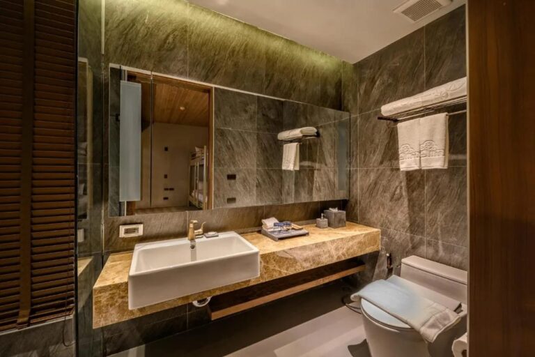 Un baño de piedra gris con lavabo sobre una encimera de mármol y un espejo grande