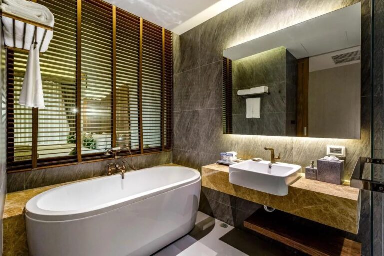 Una bañera ovalada delante de unas persianas de madera, junto a un lavabo