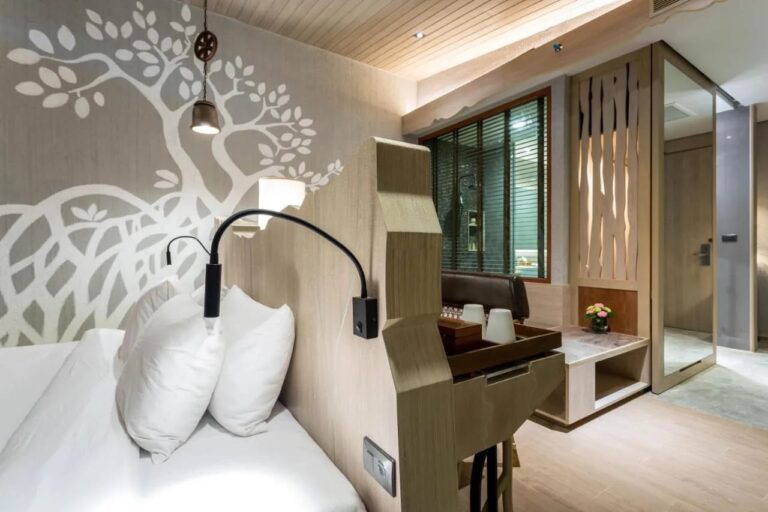 Una cama al pie de una pared pintada con un árbol blanco, con una lámpara de lectura
