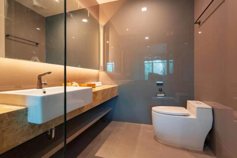 Un baño con lavabo sobre una encimera de mármol, un espejo iluminado e inodoro