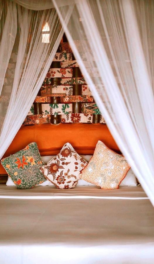Cojines de flores sobre una cama, vistos a través del mosquitero
