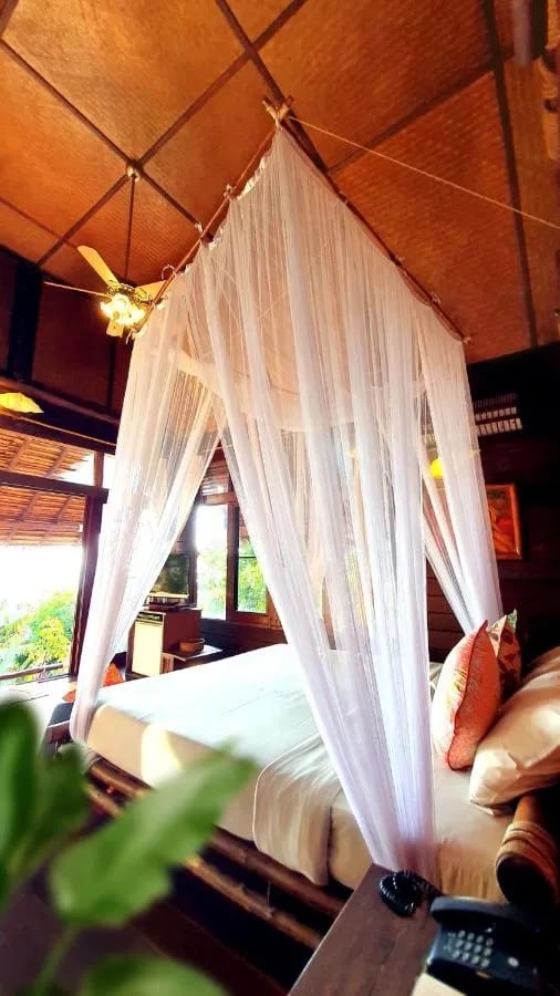 Una cama con mosquitero y un ventilador en un techo trenzado