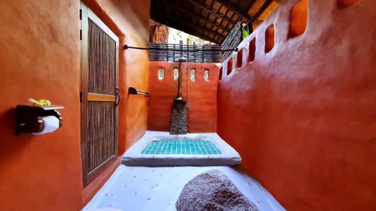 Un baño semiabierto de paredes naranjas, con una ducha sobre un suelo de mosaico turquesa