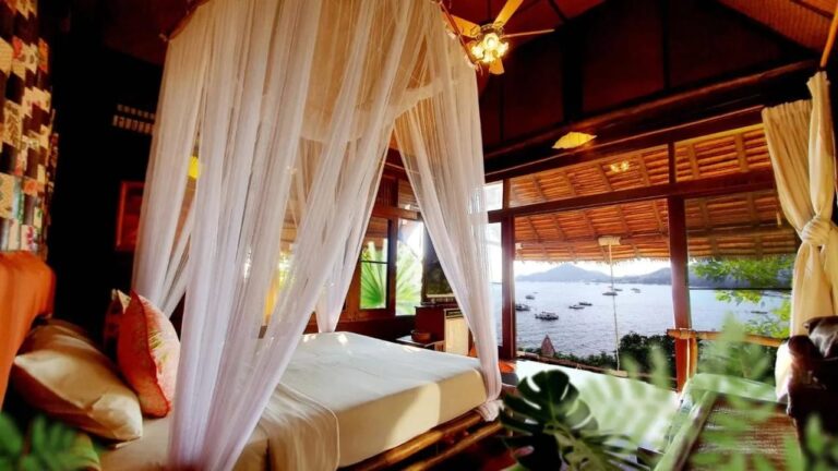 Una habitación con cama con mosquitero, abierta a la bahía y a los barcos