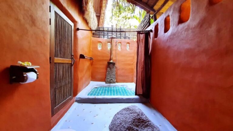 La ducha semiabierta de una cabaña, con una cortina y un suelo de mosaico turquesa