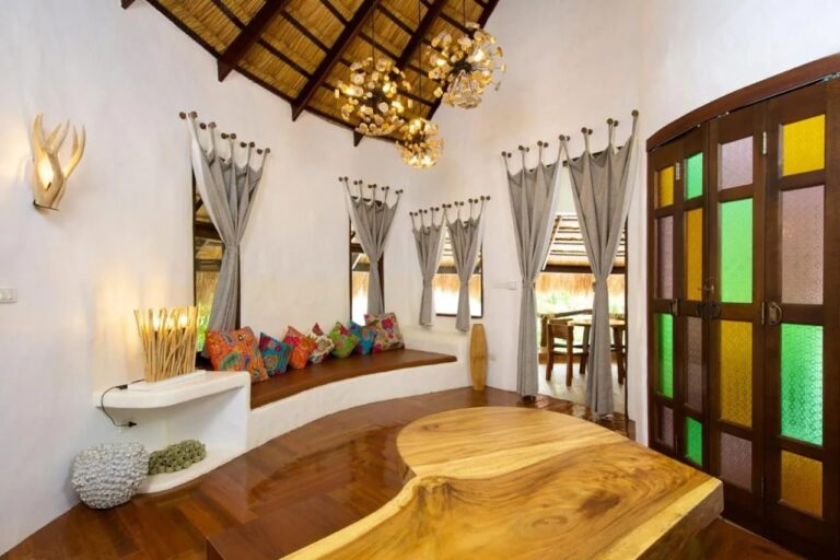 Un salón blanco con un banco de cojines de colores, una mesa de madera maciza y puertas con vitrales