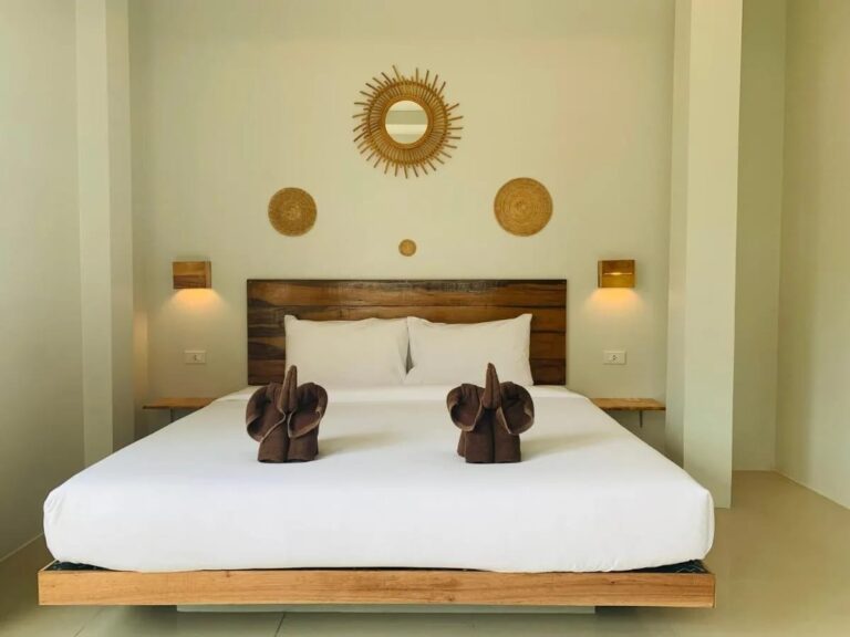 Una cama grande con cabecera de madera, elefantes hechos con toallas y un espejo sol de ratán