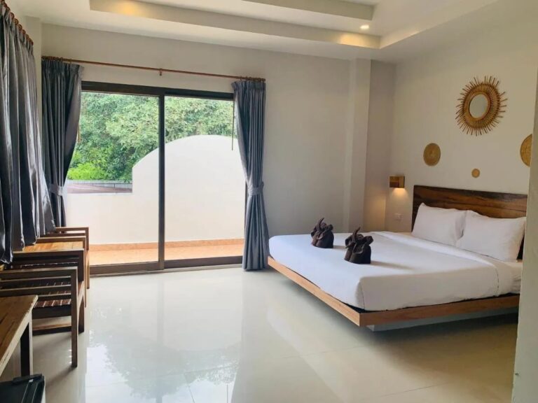Una habitación con cama grande, un ventanal que da a un balcón y sillones de madera