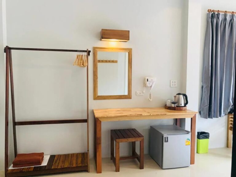 Un perchero de madera, un espejo y un escritorio con un hervidor sobre un pequeño refrigerador