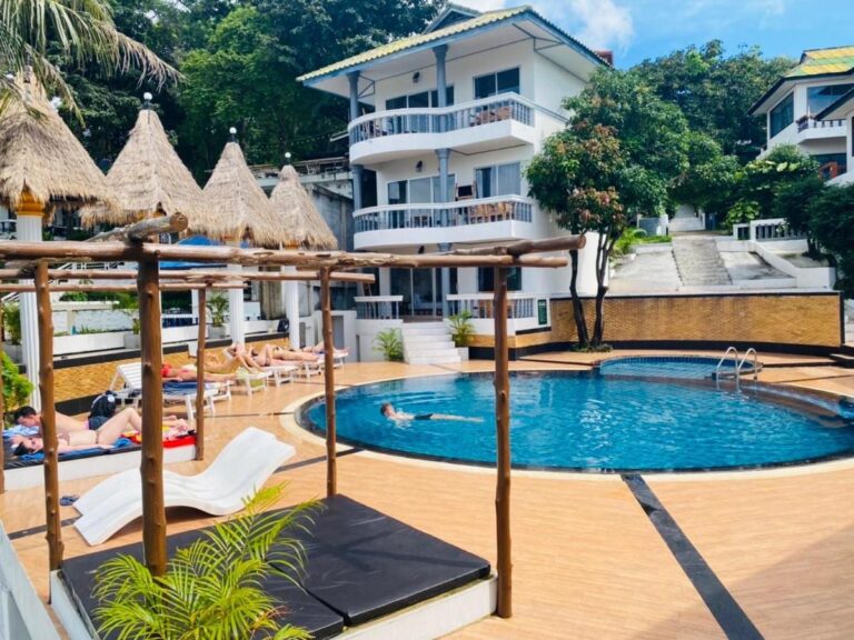 La piscina del Koh Tao Heritage, sus tumbonas y sus sombrillas de paja, delante de un edificio con balcones